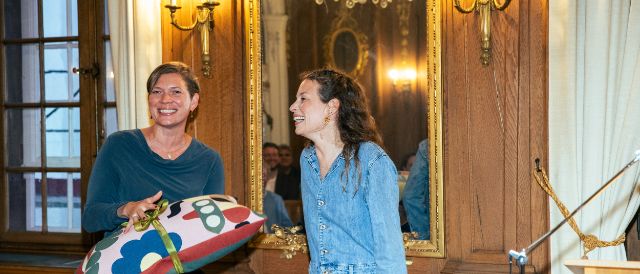 Bürgerratspräsidentin Fabienne Beyerle überreicht den symbolischen BG-Preis an die Preisträgering des BG-Preis 2025 Anna Rossinelli.